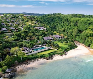 Oversigtsbillede af et resort med flere hytter, et centralt poolområde og en strand.