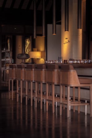 A bar area with wooden chairs and a bar counter. - Raffles Bali (Jimbaran)
