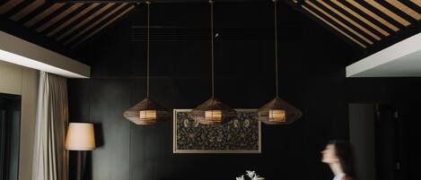 A dining area with a high ceiling, exposed beams, and a central hanging light fixture.