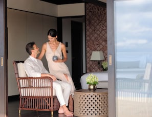 A man and a woman sitting on a wicker chair in a room with a patterned wall and a small table with a vase.