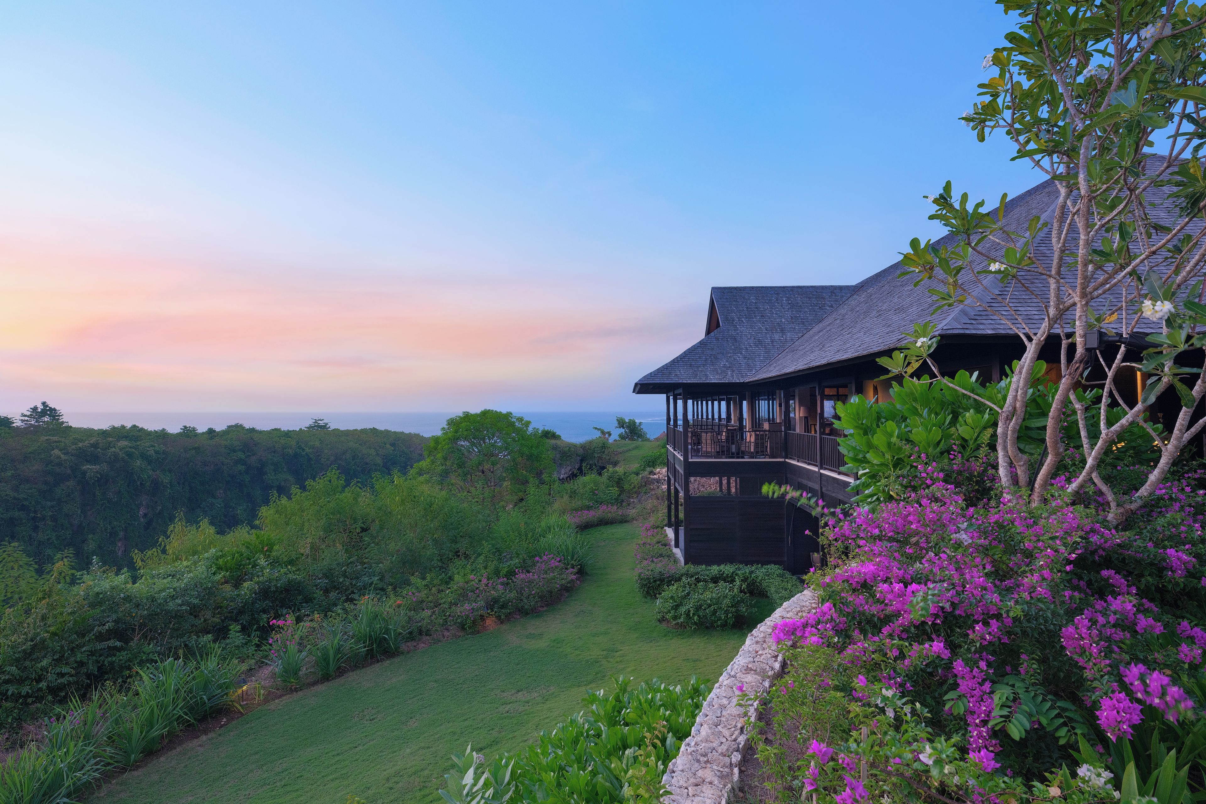 A house with a balcony overlooking a lush garden and a view of the ocean.