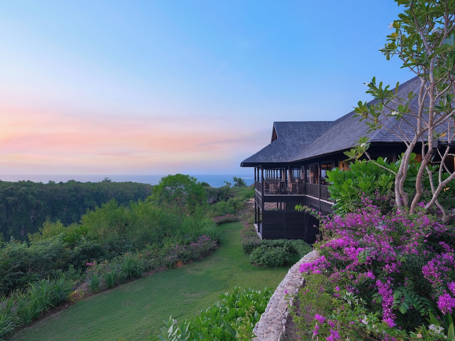 A house with a balcony overlooking a lush garden and a view of the ocean.