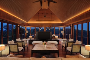A spacious living area with a large flat-screen TV, comfortable seating, and large windows offering a view of the outdoors. - Raffles Bali (Jimbaran)
