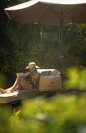 A person reclining on a lounge chair under a canopy, reading a book. - Raffles Bali (Jimbaran)