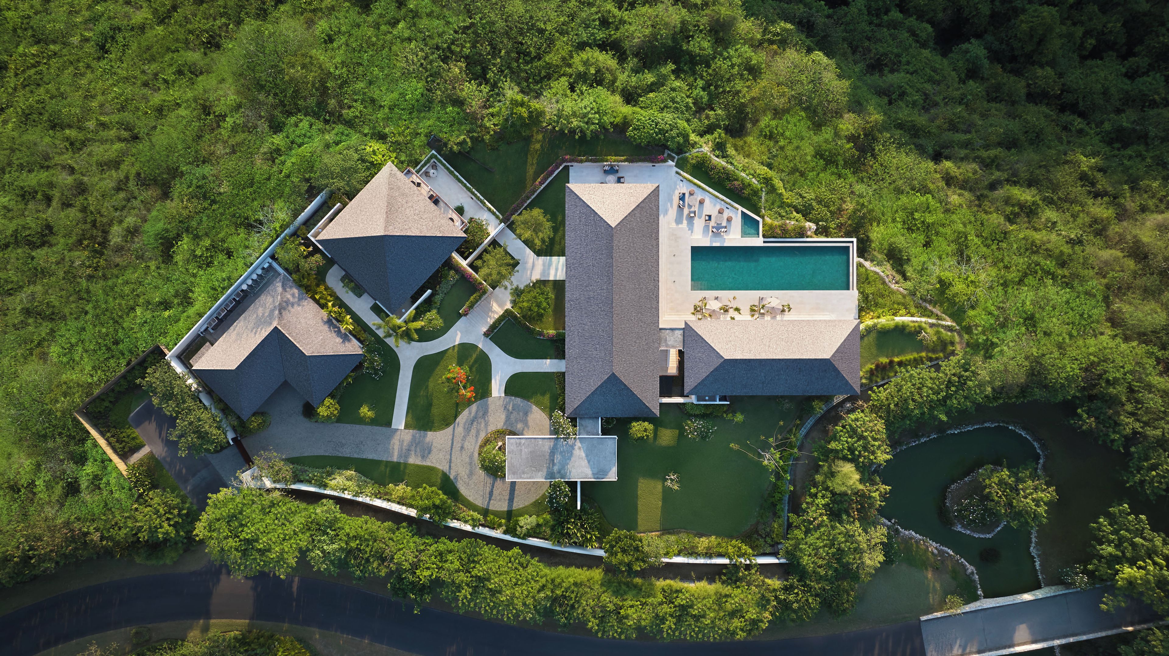Vista aérea de un moderno complejo turístico con varias edificaciones, piscina y jardines ajardinados.