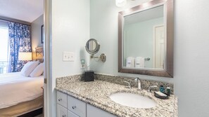 A hotel bathroom with a granite countertop, a sink, a mirror, and a small round mirror.