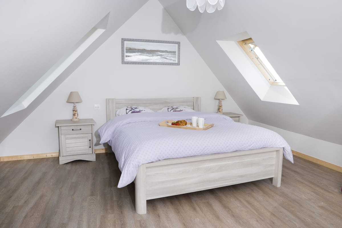 A bedroom with a sloped ceiling, a bed with a tray of breakfast items, two bedside lamps, and a framed picture on the wall.
