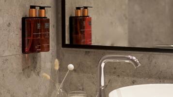 Et badeværelse med et stort spejl, en hvid vask og to shampoo flasker på væggen.