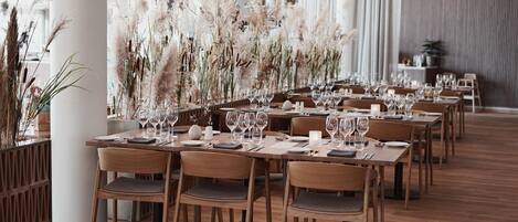 Una larga mesa de comedor dispuesta con sillas, rodeada de altas plantas decorativas.
