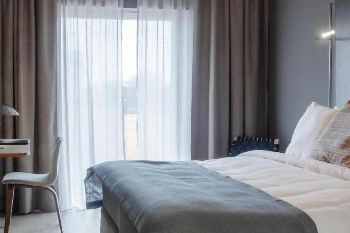 A modern hotel room with a bed, a desk, and a chair.