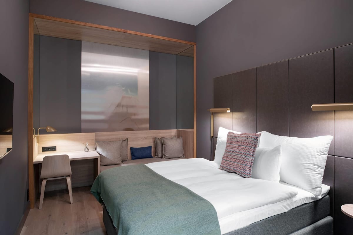 Une chambre d’hôtel moderne équipée d’un lit, d’un bureau, d’une chaise et d’un grand miroir.