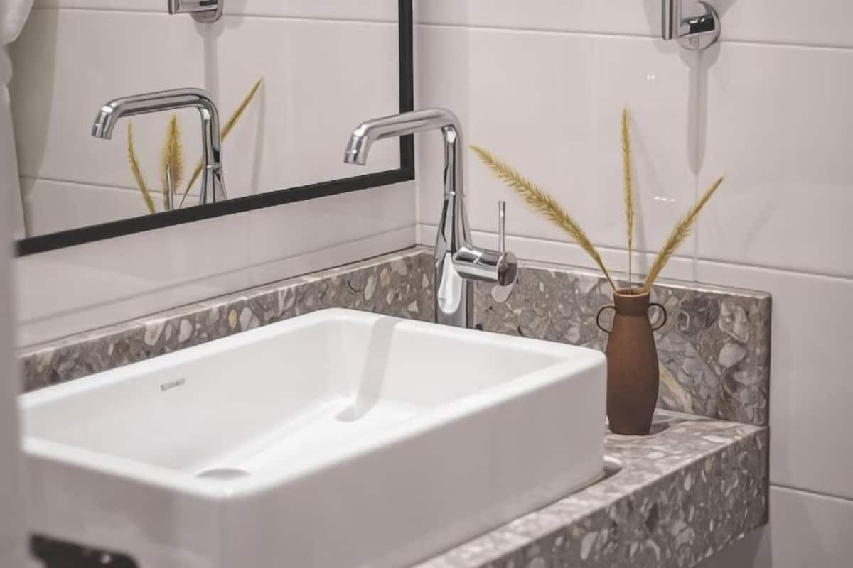 Une salle de bain avec un lavabo blanc, un miroir et un vase décoratif contenant des roseaux.
