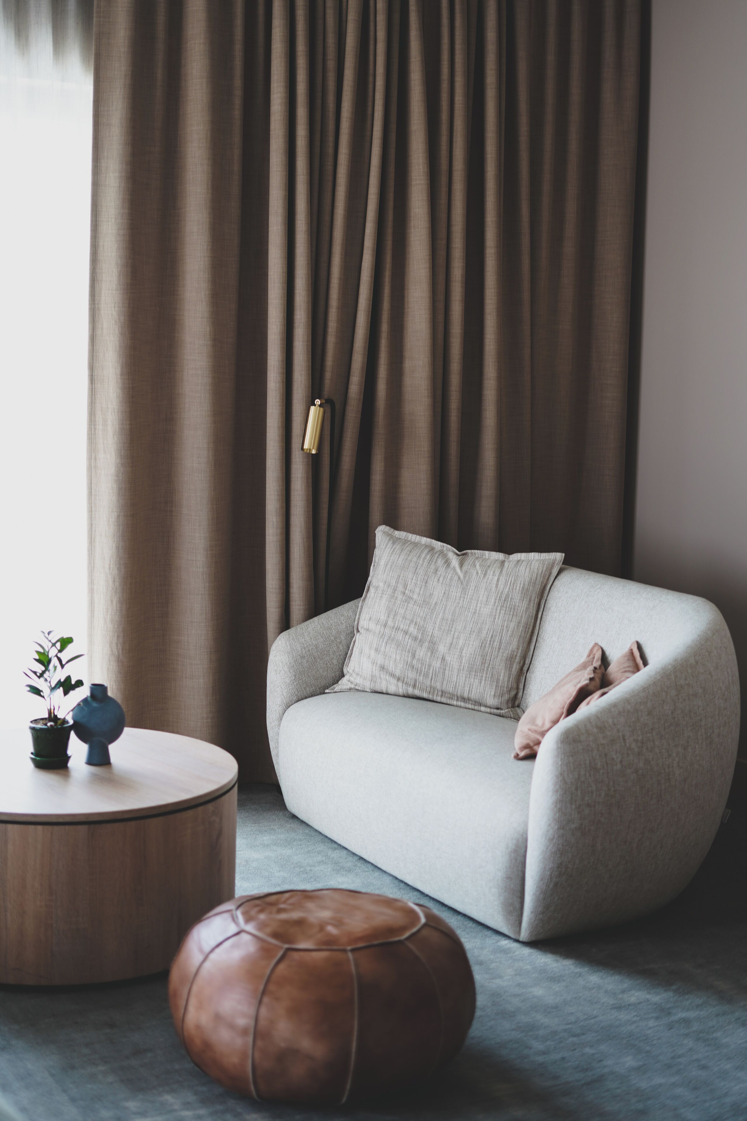 A modern living room with a grey sofa, a round wooden coffee table, a brown leather ottoman, and a potted plant.