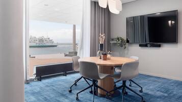 A conference room with a large table, chairs, a TV, and a view of a ship.