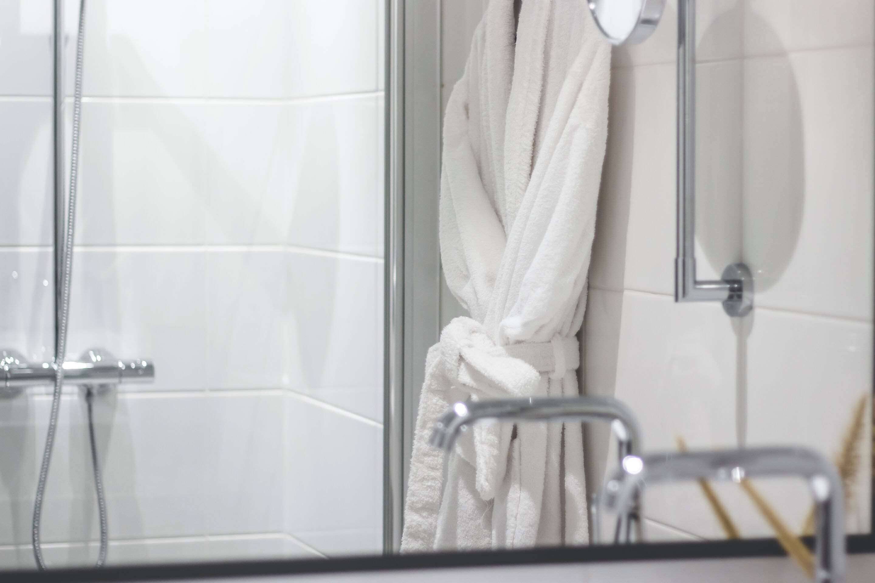 A bathroom with a glass shower enclosure, a white bathrobe hanging on a rack, and a towel rack with a towel.