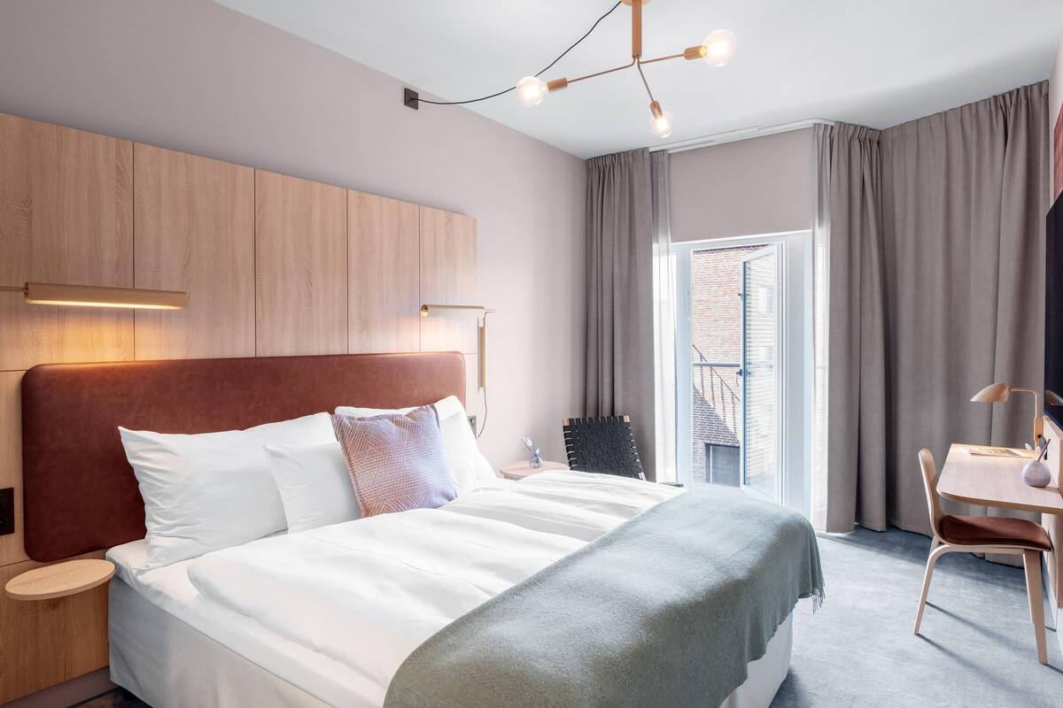 Une chambre d’hôtel moderne, dotée d’un grand lit, d’un bureau et offrant une vue sur la ville.