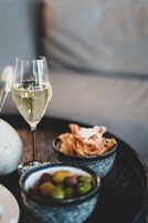 Una copa de vino blanco, un cuenco de aceitunas y un plato de pan sobre una bandeja.