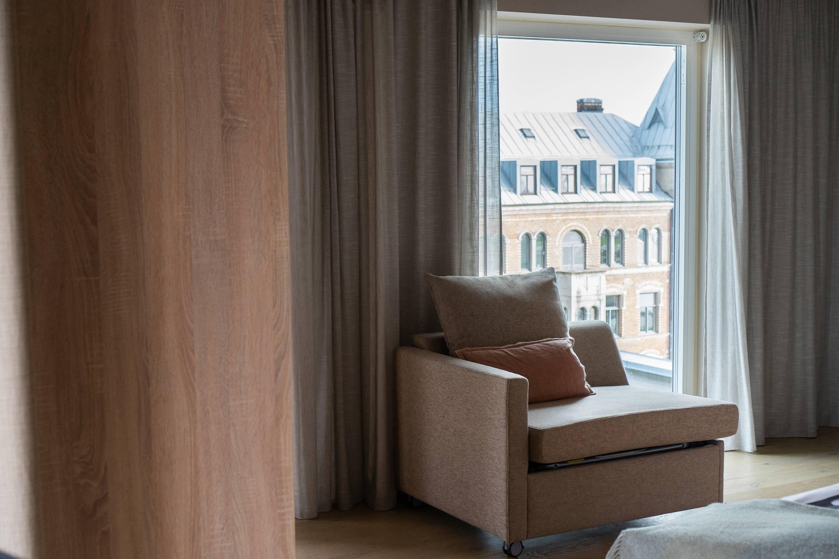 Une pièce avec une fenêtre, une chaise et une vue sur un immeuble.