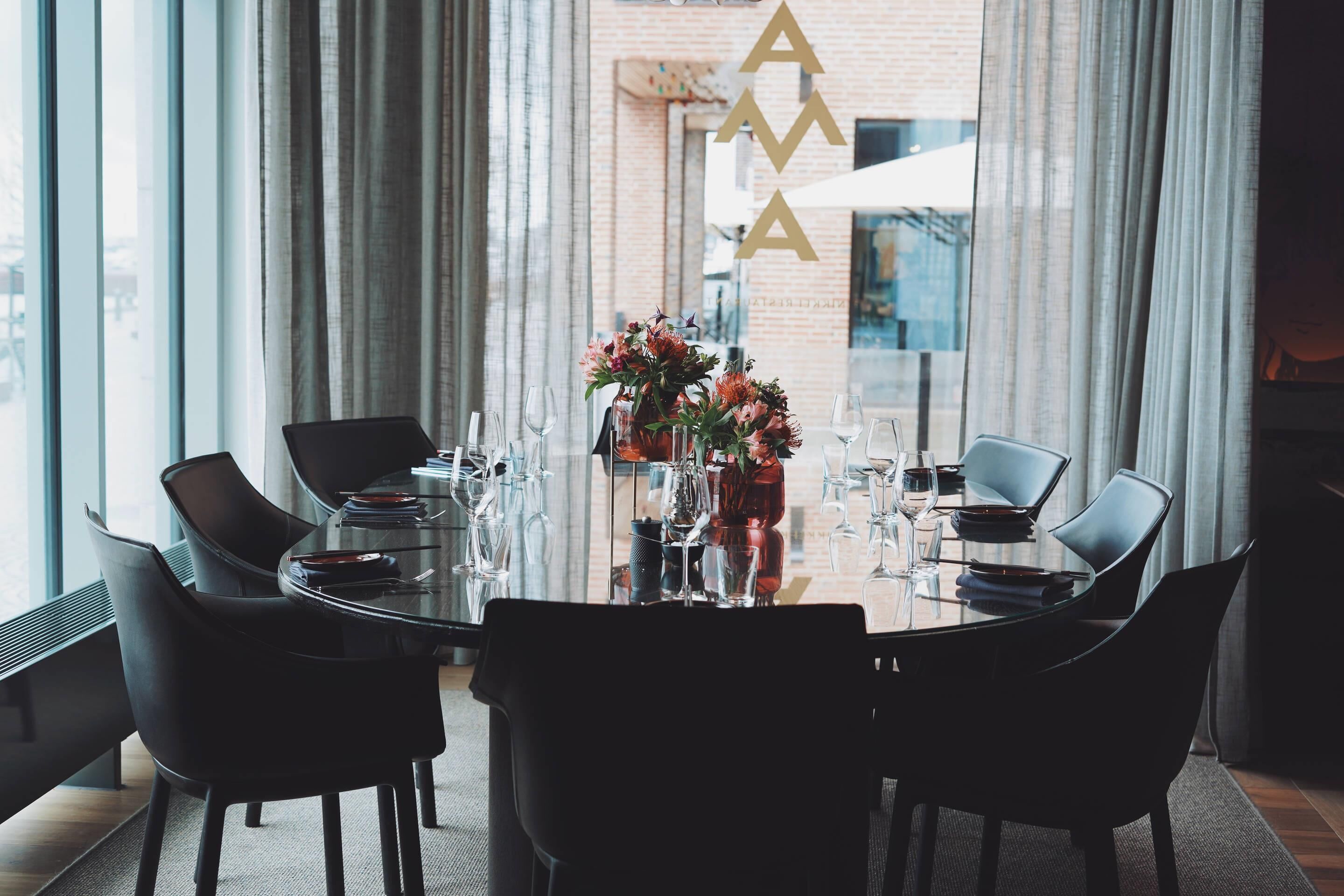 Ett modernt matområde med ett glasbord, svarta stolar och en vas med blommor.