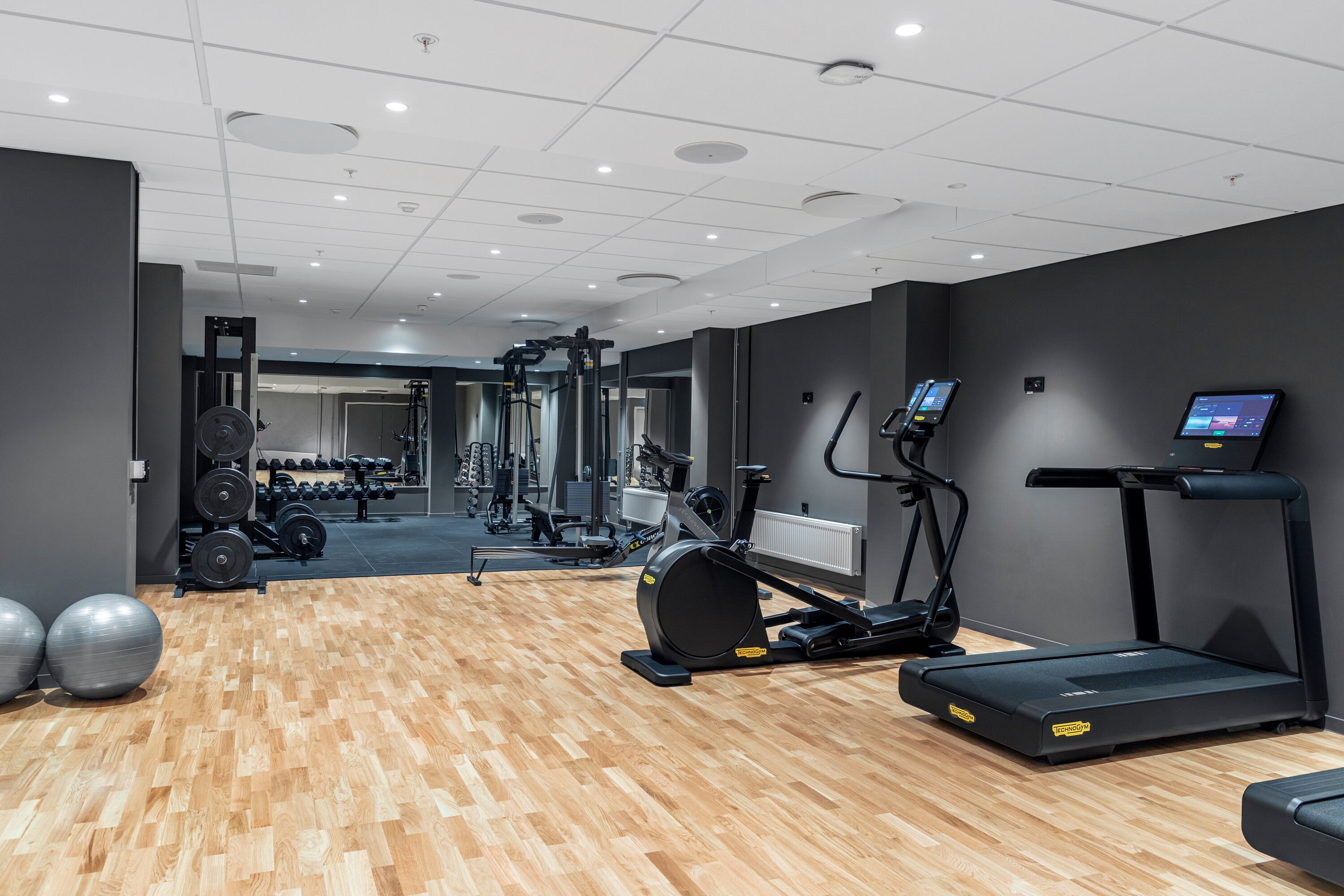 Un gimnasio con equipo de ejercicio, suelo de madera y pared espejada.