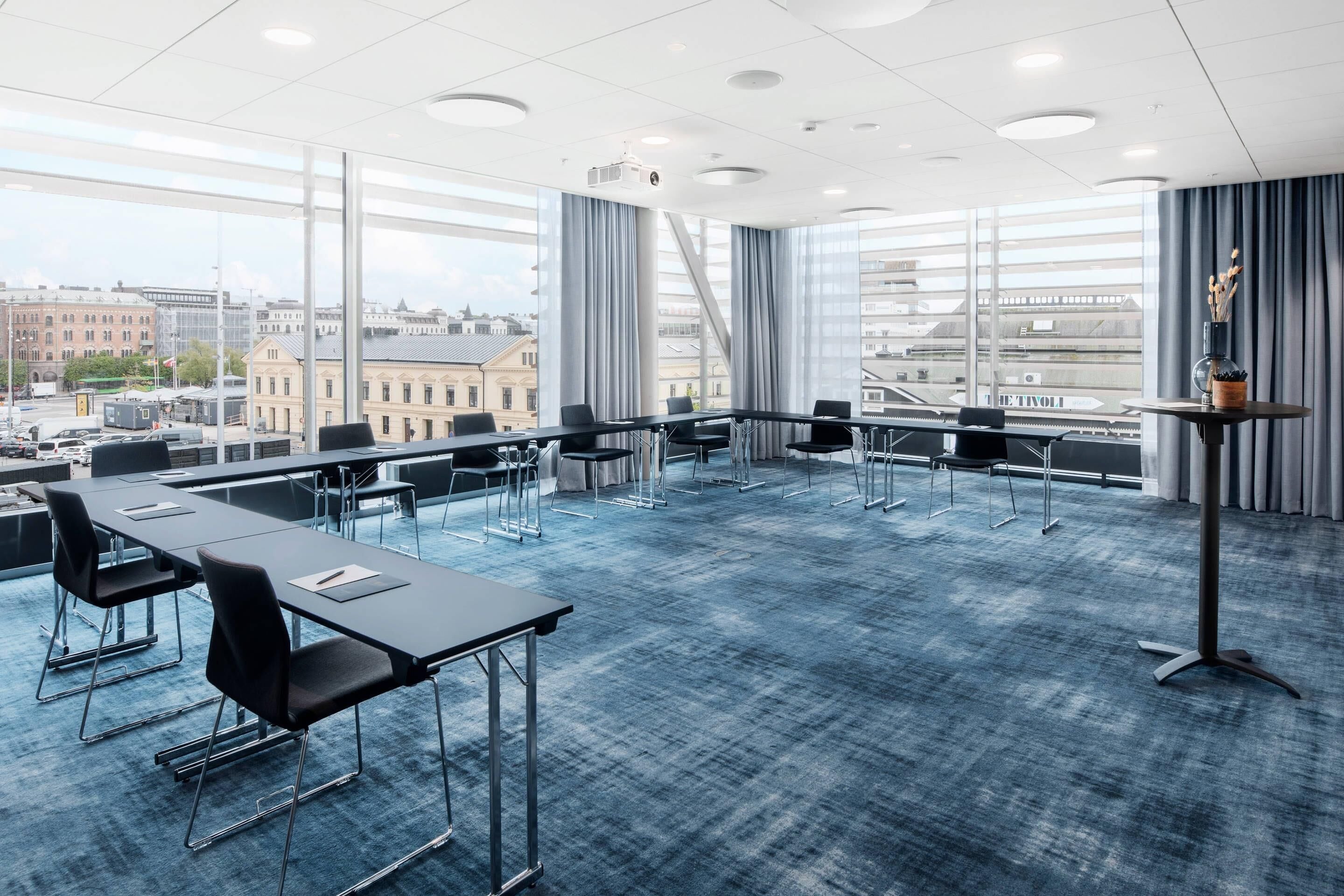 Un salón de conferencias con una gran mesa, sillas, un proyector y vistas a la ciudad a través de amplias ventanas.