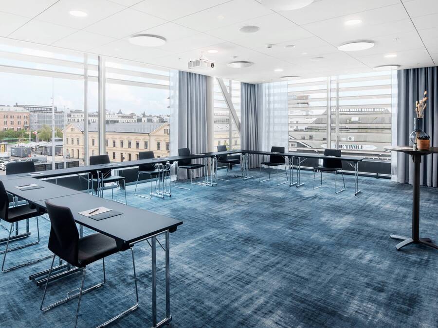 Ett konferensrum med ett stort bord, stolar, en projektor och utsikt över stadsbilden genom stora fönster.