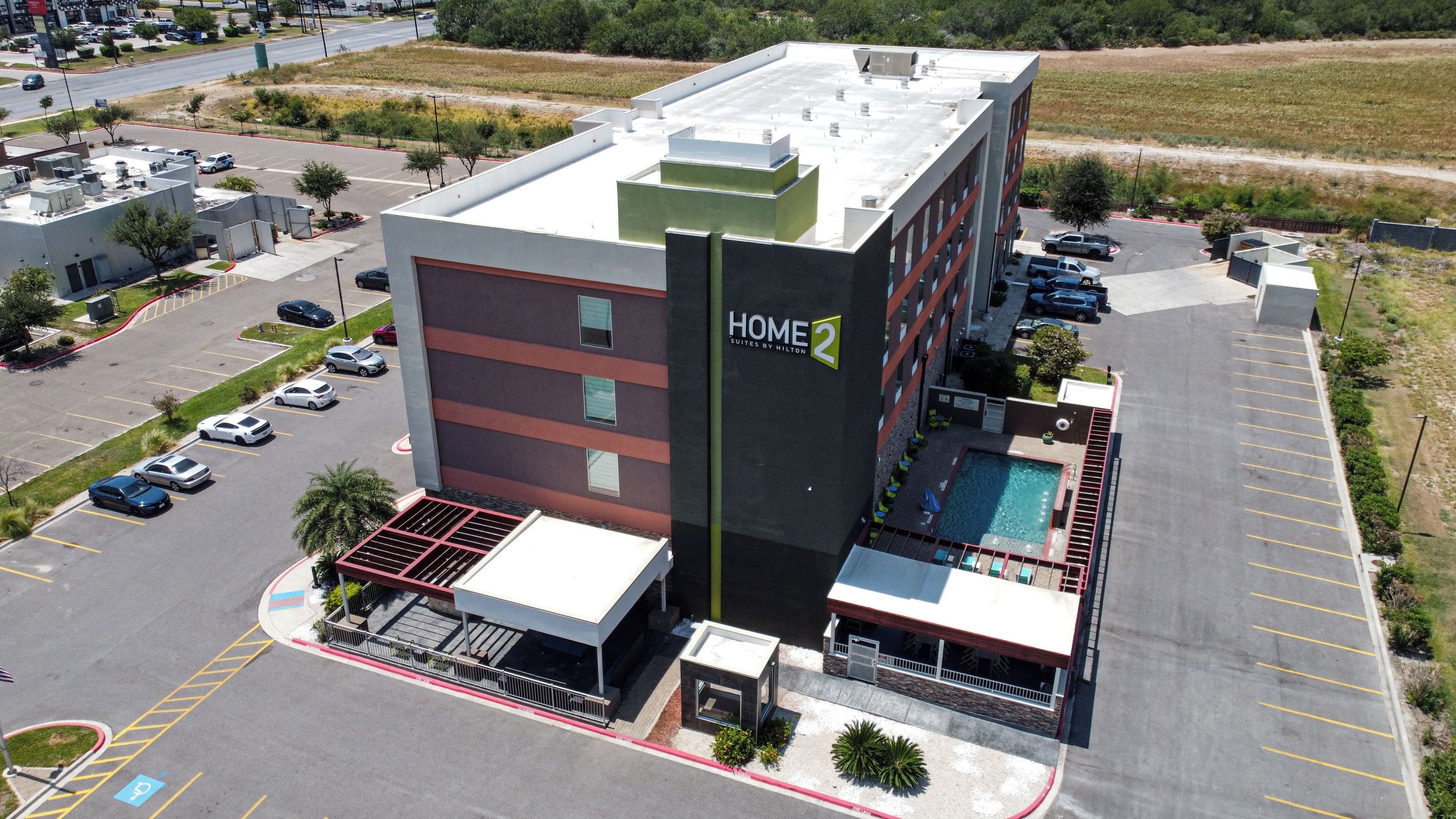 A hotel with a rooftop pool, a parking lot, and a sign indicating it's a Hilton Suites hotel.
