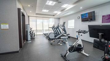 Un gimnasio con bicicletas estáticas, cintas de correr y un televisor instalado en la pared.