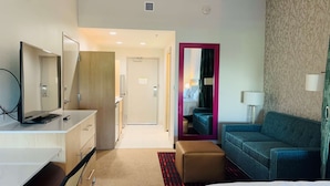 A hotel room with a bed, a desk with a computer, a chair, a sofa, and a small table with a lamp.