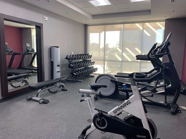 A gym with a spinning bike, treadmills, and dumbbells. - Home2 Suites by Hilton Edinburg, TX (Edinburg)