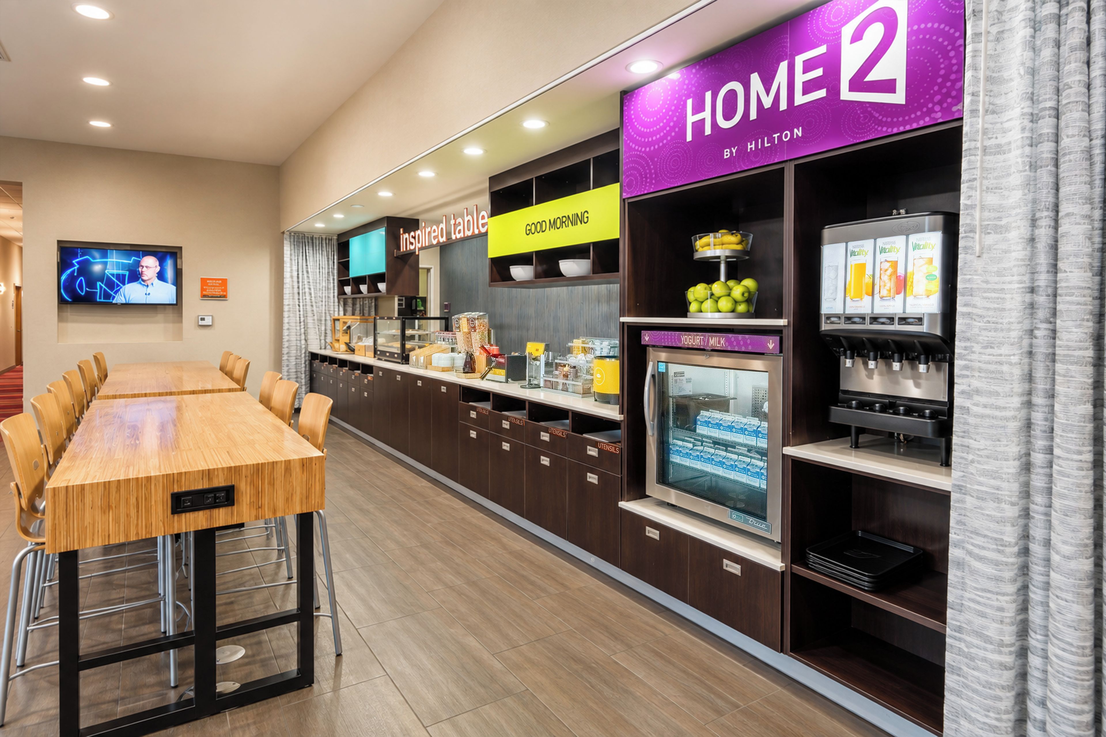 A hotel breakfast area with a long counter, a television screen, and a vending machine.