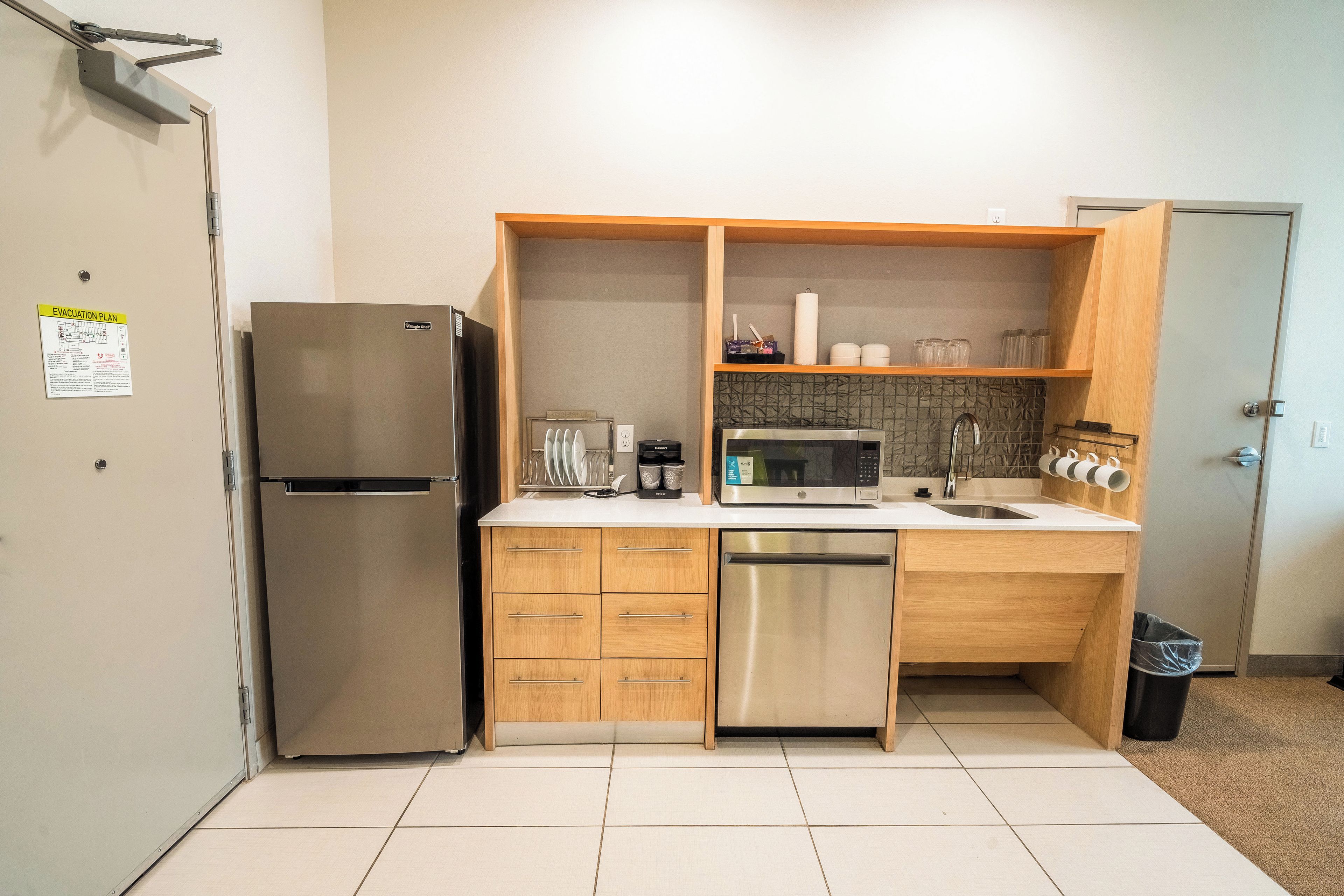 Cocina compacta con refrigerador, microondas, lavavajillas y armarios de madera.