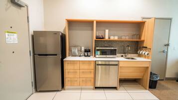 Cocina compacta con refrigerador, microondas, lavavajillas y armarios de madera.