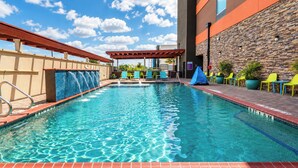 A swimming pool with a clear blue water surface, surrounded by a brick deck and a stone wall.