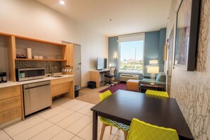 A modern kitchen with a microwave, sink, and wooden cabinets. There is a dining area with a table and chairs, and a window with a view of the outside. - Home2 Suites by Hilton Edinburg, TX (Edinburg)