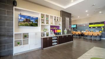 A hotel lobby with a reception desk, a coffee and tea station, and a dining area with tables and chairs.