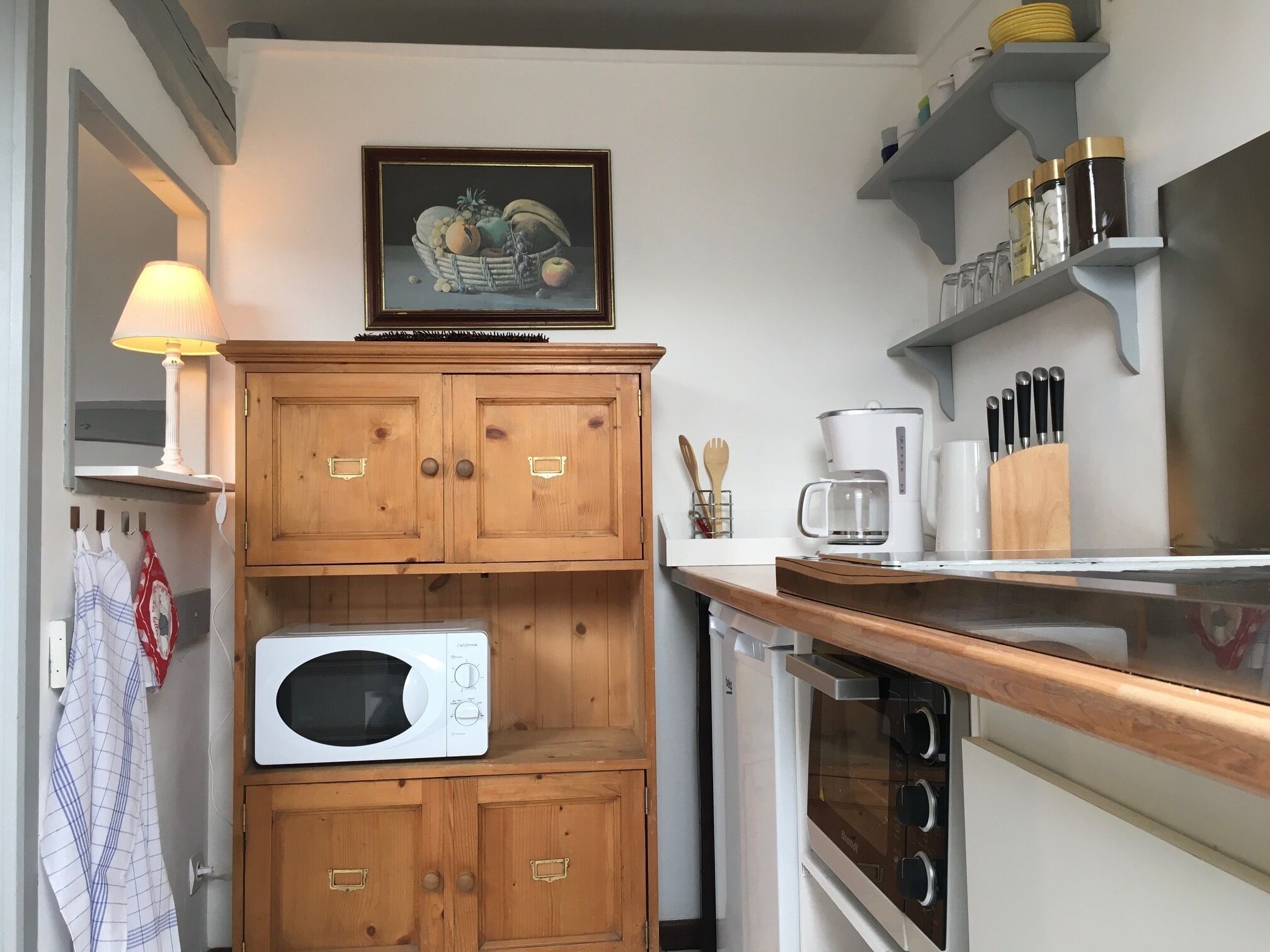 A kitchen with wooden cabinets, a microwave, an oven, a coffee maker, and a framed fruit still life on the wall.