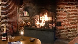 Una chimenea de ladrillo con fuego, una botella de champán, dos copas y un bol sobre una mesa redonda.