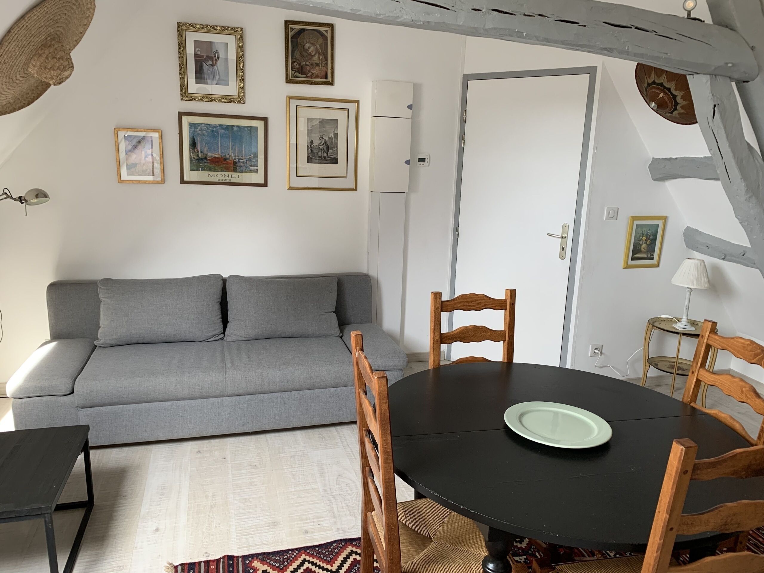 A living room with a grey sofa, a round wooden table with chairs, and framed artwork on the walls.