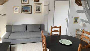 A living room with a grey sofa, a round wooden table with chairs, and framed artwork on the walls.