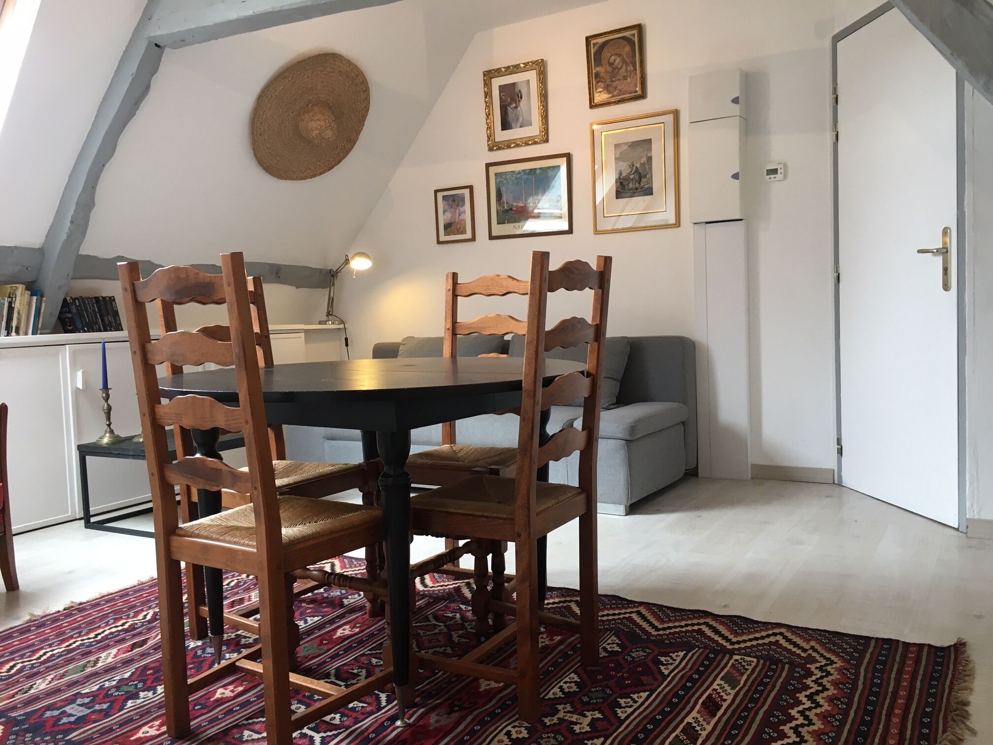 Un comedor con una mesa redonda, sillas de madera, un tapete estampado y una cocina al fondo.