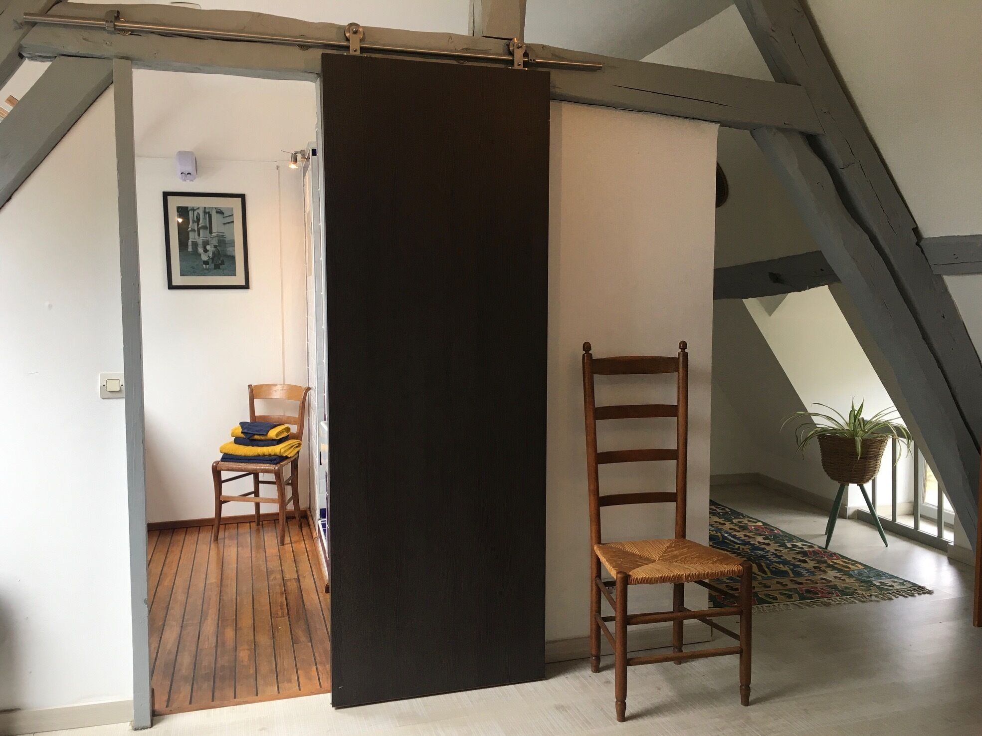 A room with a wooden chair, a black partition, and a framed picture on the wall.