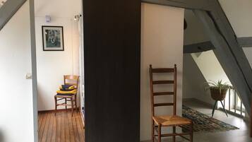 A room with a wooden chair, a black partition, and a framed picture on the wall.