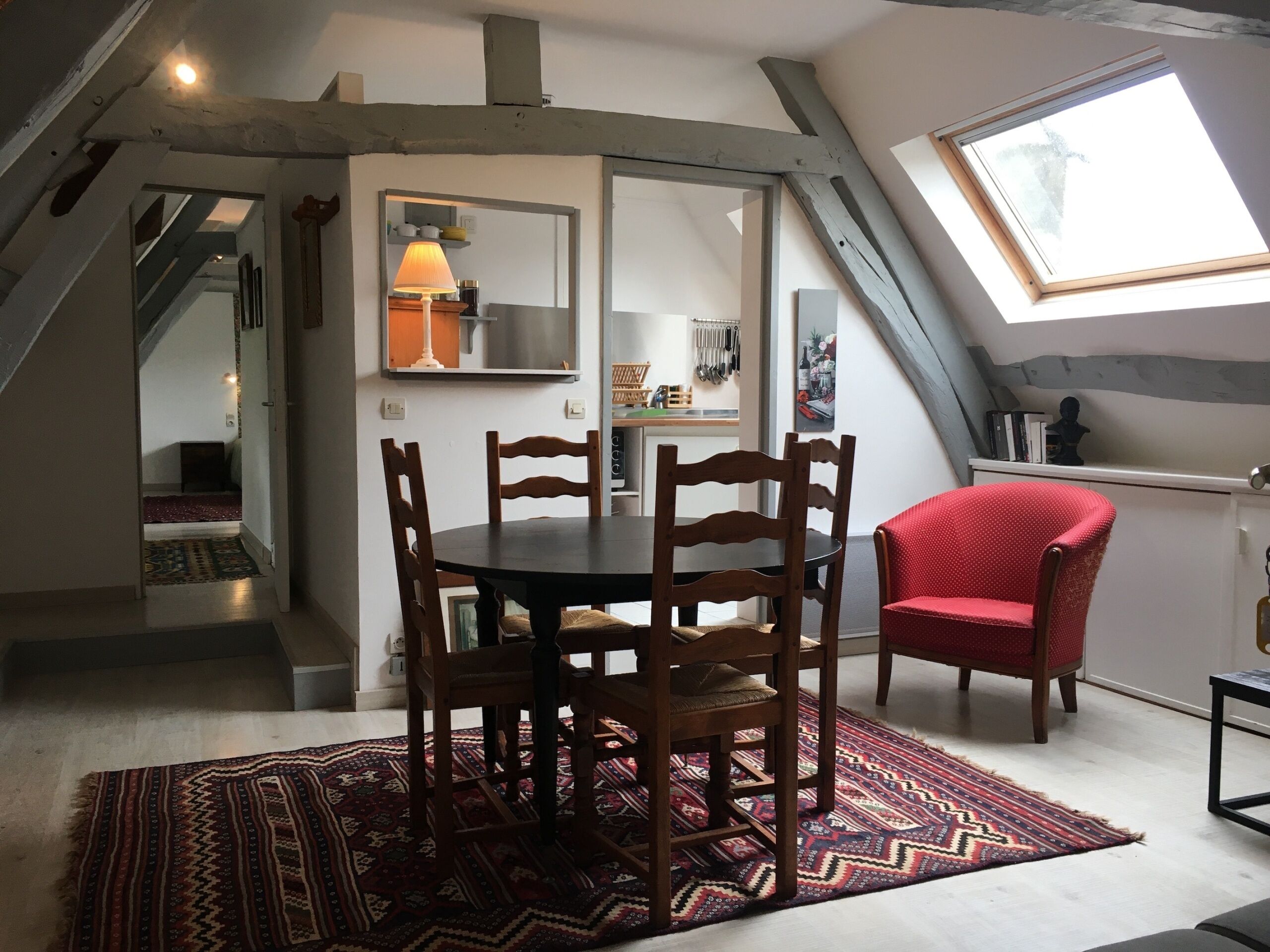 Een eetruimte met een ronde tafel, houten stoelen en een rode stoel. Op de vloer ligt een tapijt met een patroon.