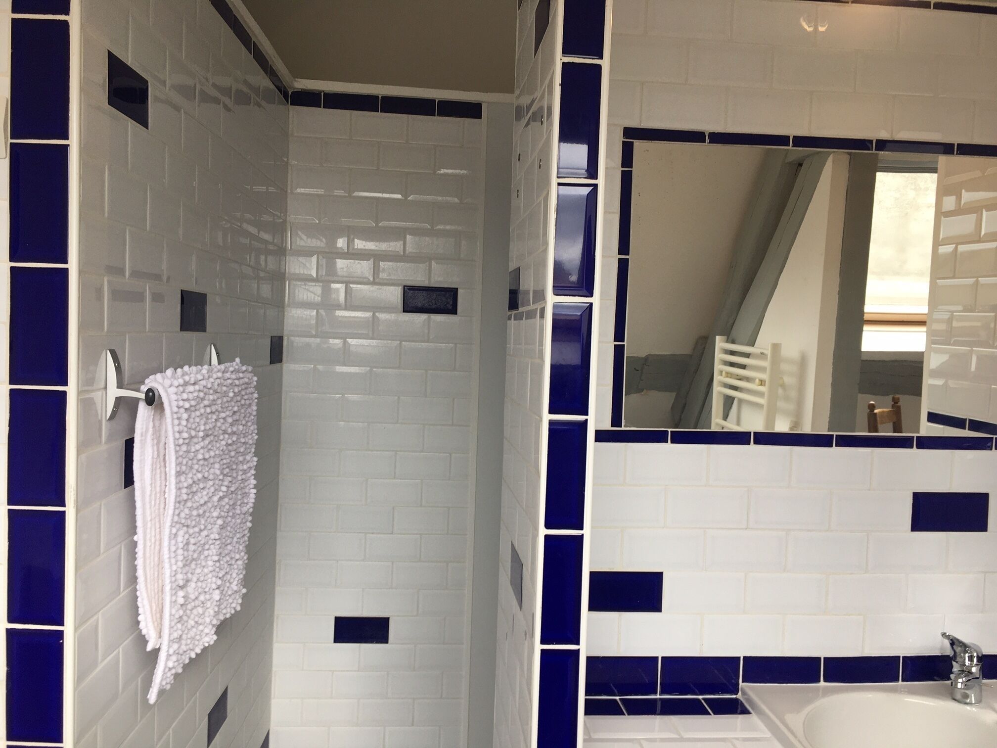 A bathroom with white and blue tiles, a white towel hanging on a rack, and a mirror reflecting a staircase.