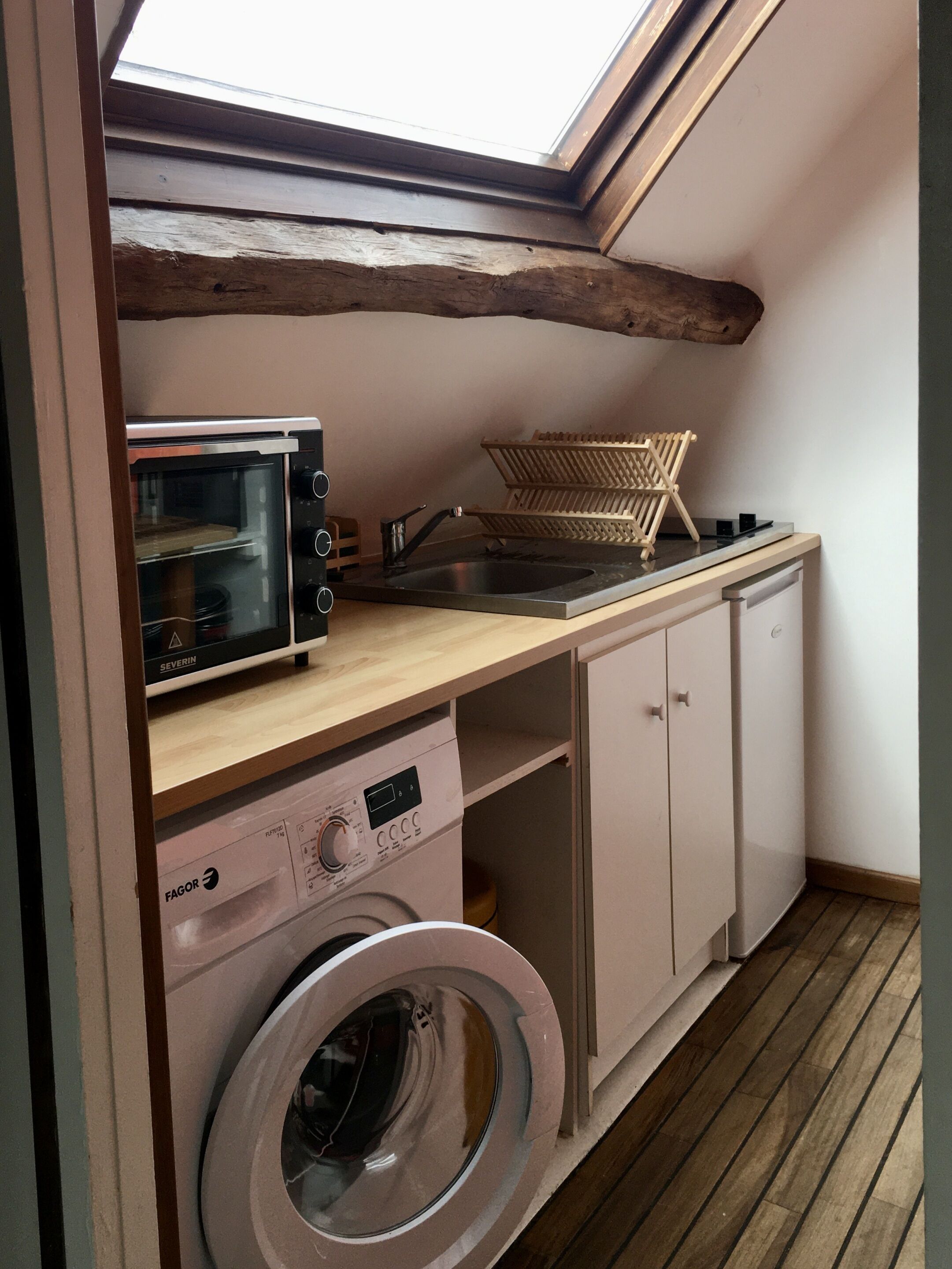 Une cuisine compacte équipée d’un lave-linge intégré, d’un four grille-pain et d’un étendoir.