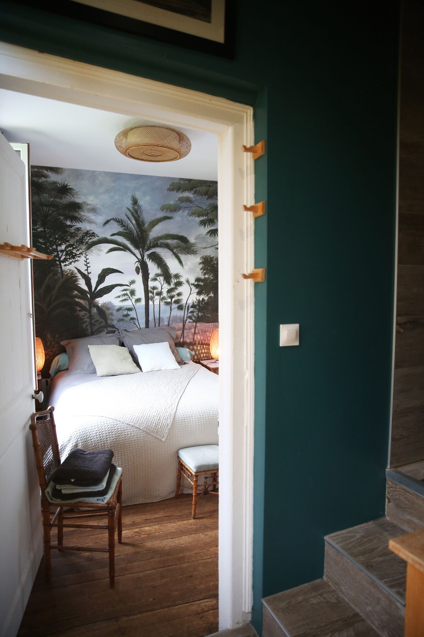 A bedroom with a bed, pillows, a chair, and a nightstand. There is a staircase leading to another level.