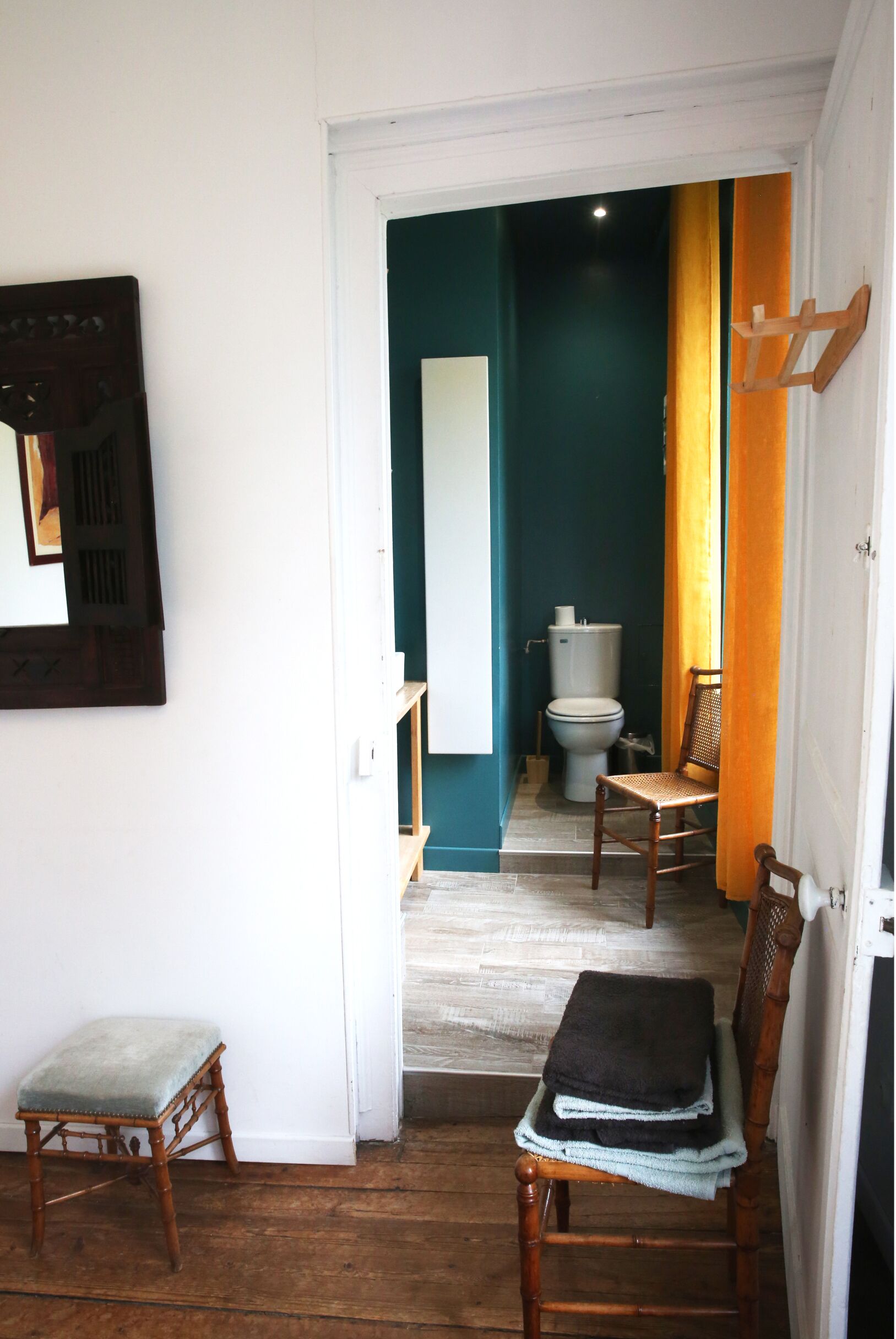 A narrow hallway leading to a bathroom with a toilet, a chair, and a bench.