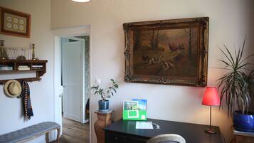 A room with a desk, a chair, a bench, a potted plant, a framed painting, and a lamp.