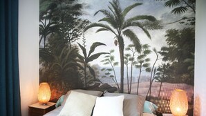 Un dormitorio con un mural tropical, dos lámparas de noche y una cama con almohadas.